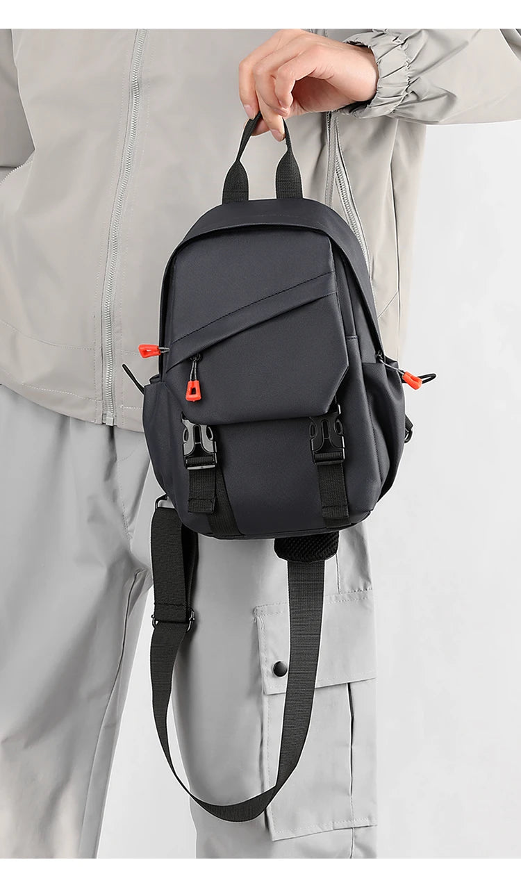 Un sac de sport pour homme gris foncé est tenu par une main contre un vêtement gris clair.