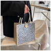 A beige floral linen tote bag with blue and white pattern is held by a person in a black suit jacket.