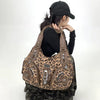 A person wearing a black hat and black shirt holds a brown leopard print crossbody shoulder bag.