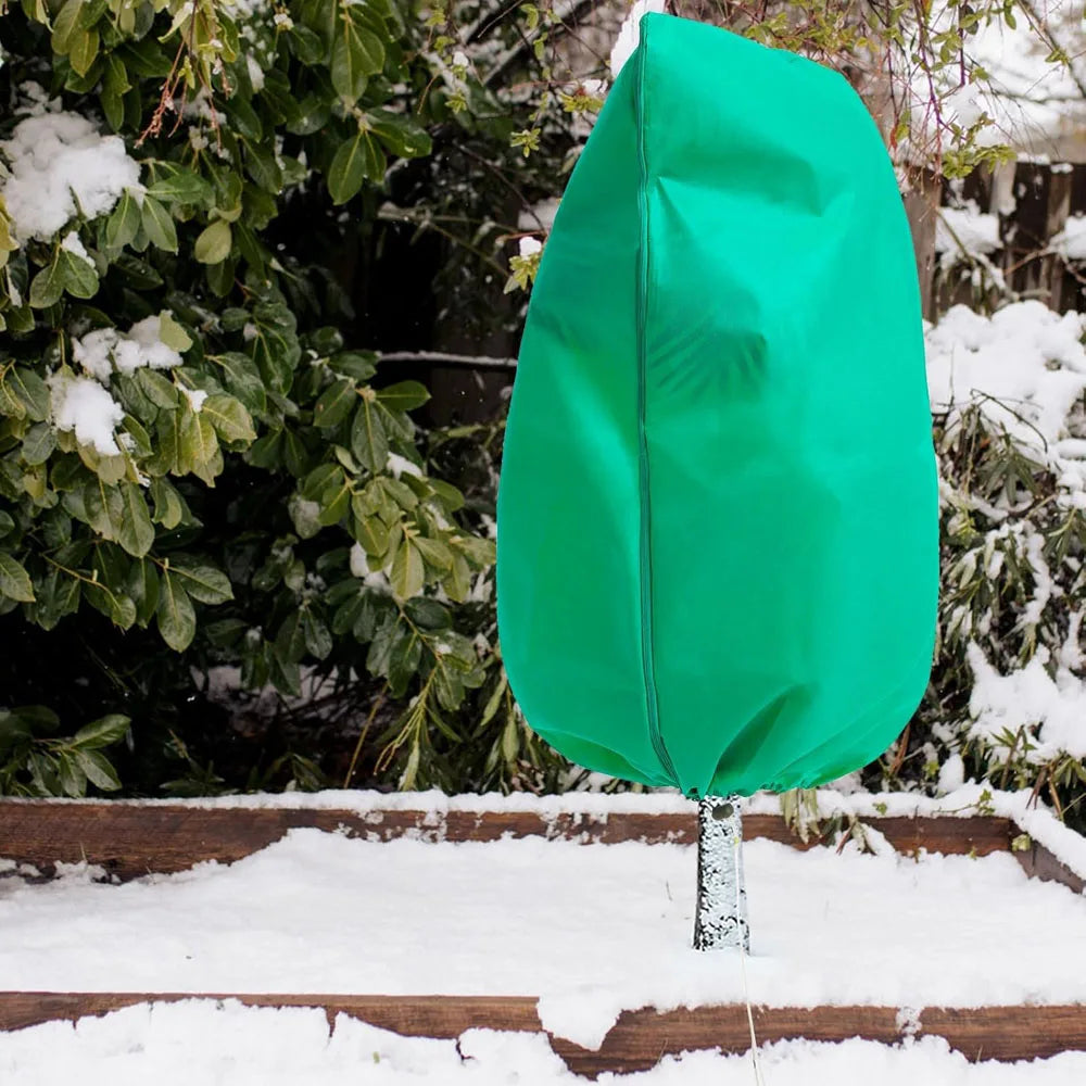 A bright green plant protection cover with a zipper is displayed outdoors on a wooden frame covered in snow.