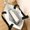 A white reusable tote bag with black handles holds a rectangular box.