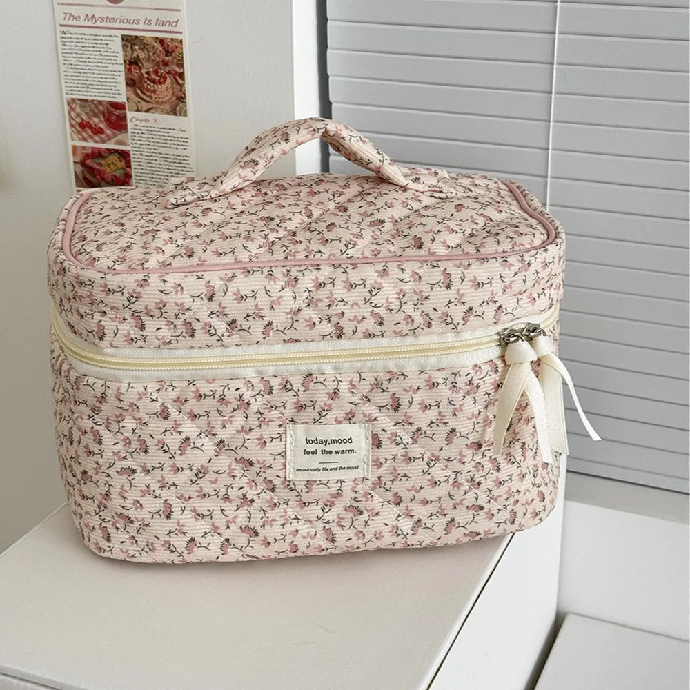 A pink floral print quilted cosmetic bag with a fabric handle and drawstring closure resting on a white surface.