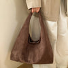 A brown suede shoulder tote bag being held by a person wearing light-colored pants.