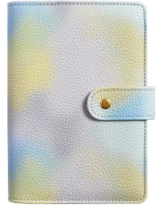 A light purple and yellow watercolor patterned leather notebook cover with a gold snap closure.