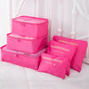 A set of pink mesh packing cubes and laundry pouches for travel organization displayed on a white bed.