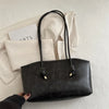 A black PU leather tote bag with black handles resting on a white textured surface.
