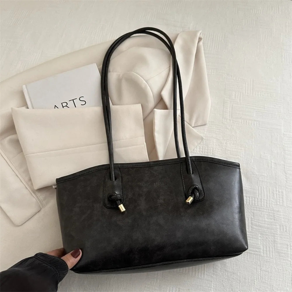 A black PU leather tote bag with black handles resting on a white textured surface.
