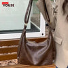 A brown vintage PU leather tote bag with a gold-toned crossbody strap resting on a wooden surface.