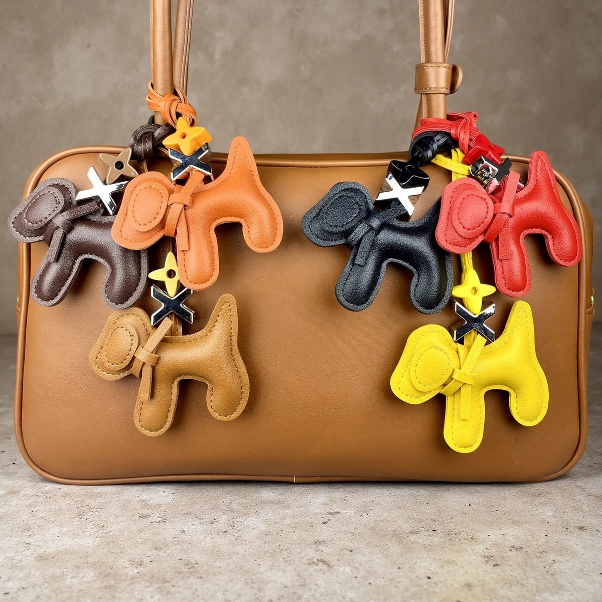 A tan PU leather bag features multiple puppy charms with bow ties hanging from the strap.