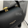 A close-up of a black leather shoulder bag with gold hardware and a gray fabric background.