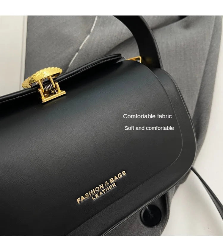A close-up of a black leather shoulder bag with gold hardware and a gray fabric background.