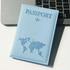 A light blue leather passport holder with a world map design is placed next to a silver laptop and a black keyboard.