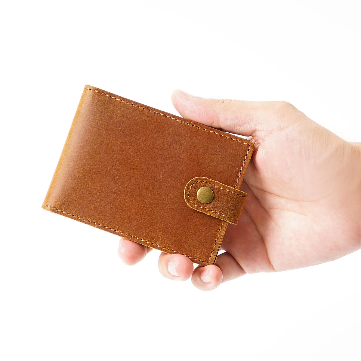 Une main tient un portefeuille bi-plis en cuir brun et authentique pour les pièces d'identité et cartes.