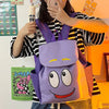 A person holds a purple Dora The Explorer cartoon flannel backpack against an orange background.