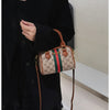 A woman holds an elegant leather tote diaper bag with a crossbody strap against a dark coat.