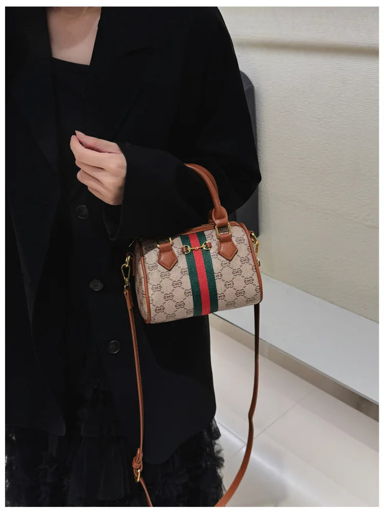 A woman holds an elegant leather tote diaper bag with a crossbody strap against a dark coat.