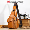 A brown leather sling backpack with a dark strap and a Singer sewing machine is displayed on a wooden surface.