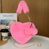 A bright pink faux fur heart shaped crossbody purse with gold chain details.