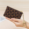 A hand holds a brown geometric mini coin purse with a gold chain.