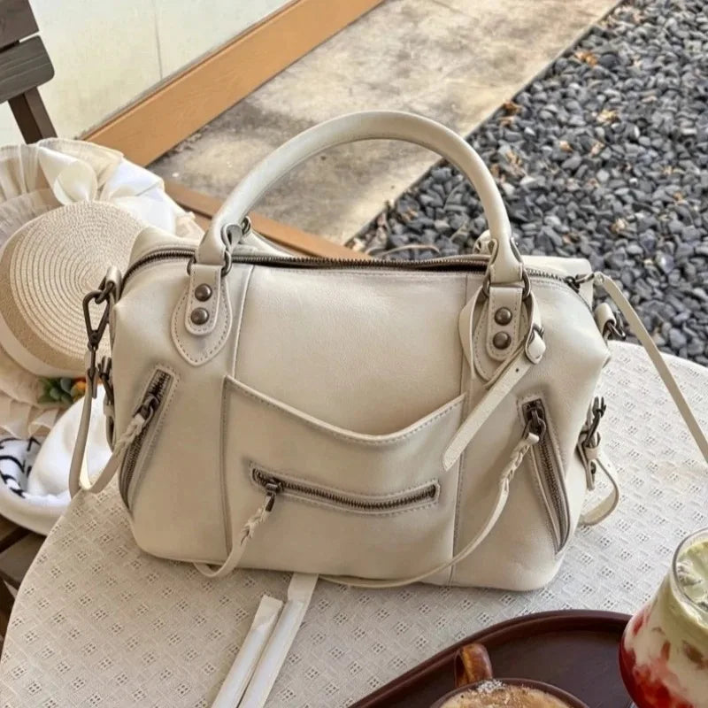 A cream-colored retro motorcycle PU leather crossbody shoulder bag resting on a white cloth.