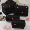 A set of black quilted cosmetic bags with pink bows and a white lampshade in the background.
