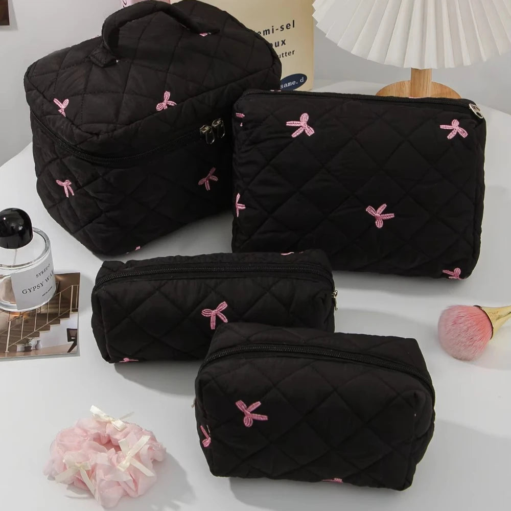 A set of black quilted cosmetic bags with pink bows and a white lampshade in the background.