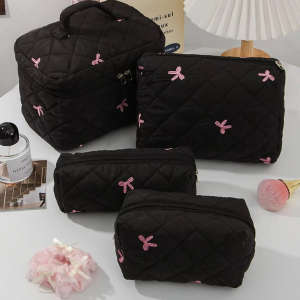 A set of black quilted cosmetic bags with pink bows and a white lampshade in the background.