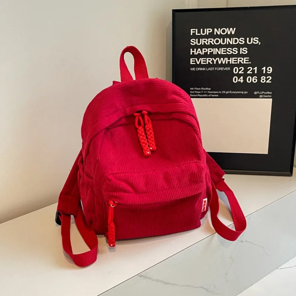 A bright red corduroy daily backpack resting on a white surface.