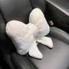 A white, fluffy bowknot car headrest pillow with lumbar support resting on a dark gray leather seat.