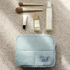 A light blue quilted puffer makeup bag with several brushes and bottles displayed on a beige textured surface.