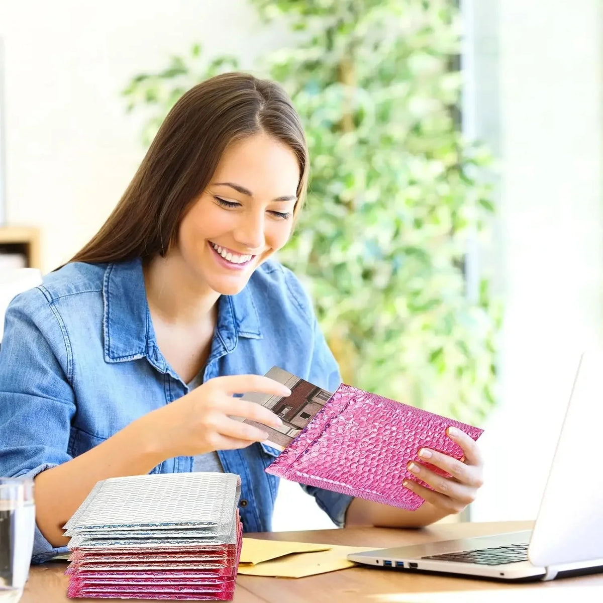 A woman is sealing holographic bubble mailers with a self-seal closure on a wooden table.