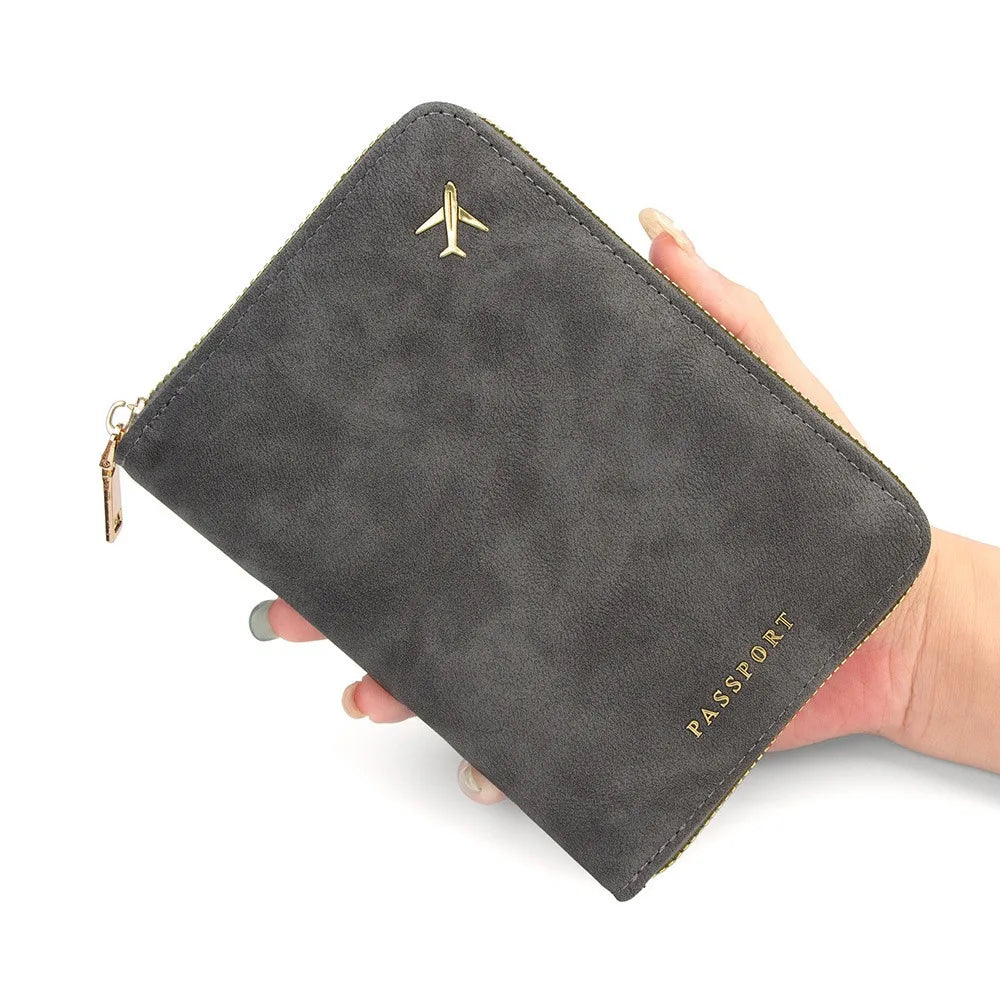 A dark gray slim passport wallet with a gold airplane emblem is held in a hand.