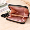 A pink and gold striped PU leather compact wallet with a black zipper closure and tassel resting on a wooden surface.