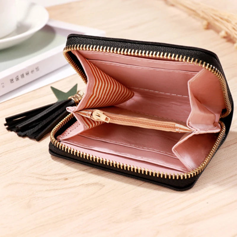 A pink and gold striped PU leather compact wallet with a black zipper closure and tassel resting on a wooden surface.