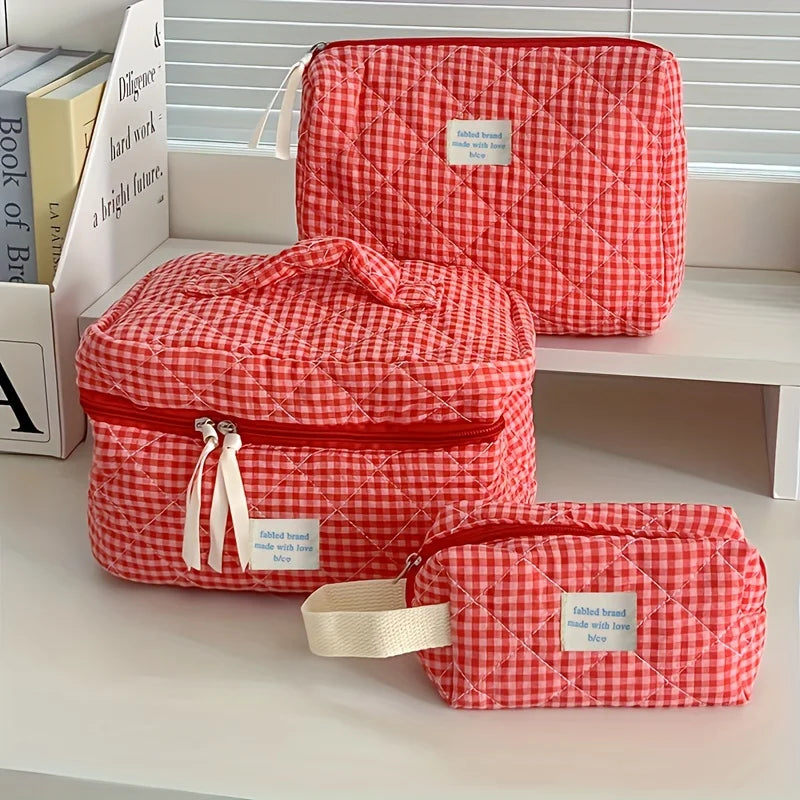 A red and white plaid cosmetic storage bag is displayed on a white shelf.