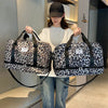 A woman holds a black leopard print travel duffel bag with shoe compartments in front of her.