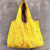 A bright yellow foldable reusable shopping bag with a mesh top is displayed against a gray concrete background.