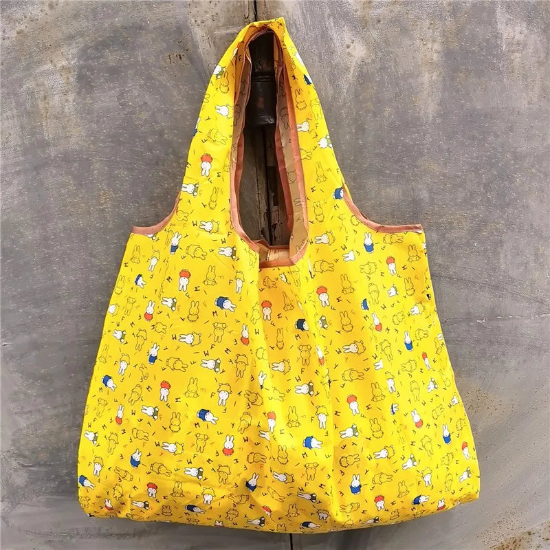 A bright yellow foldable reusable shopping bag with a mesh top is displayed against a gray concrete background.