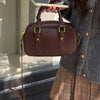 A brown vintage PU leather shoulder bag with gold hardware being held by a person against a light background.