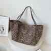 A brown leopard print canvas crossbody tote bag hanging on a white pedestal.
