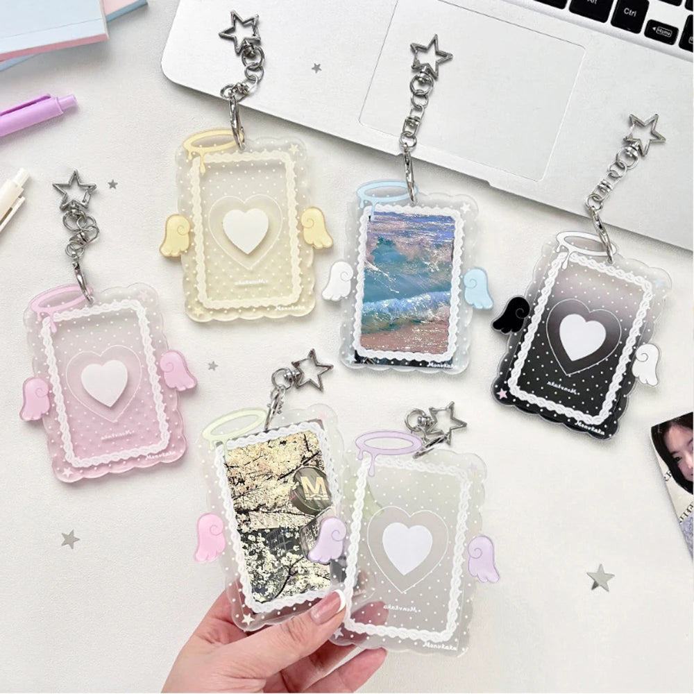 A hand holds several clear acrylic photocard holders with decorative wings and heart cutouts.