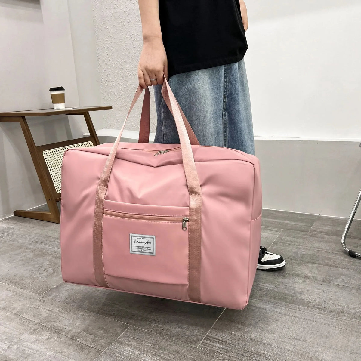 A pink canvas travel storage bag with a shoulder strap is held by a person in a modern indoor setting.