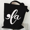 Black canvas tote bag featuring a white script design of 'la' with a ghost and pumpkin motif.