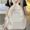A light beige backpack with a bow detail and white lace trim is worn by a person.