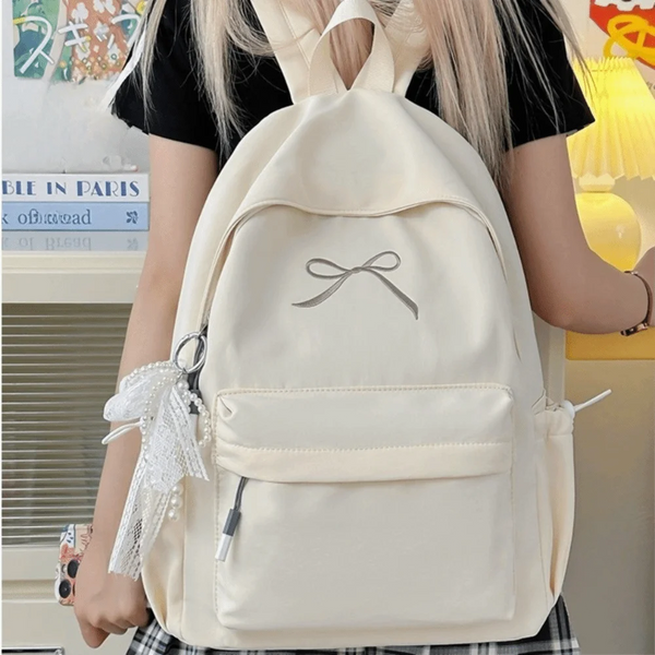 A light beige nylon backpack with a bow detail and white lace trim worn by a person.