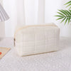 A cream-colored quilted velvet cosmetic and toiletry bag resting on a white textured surface.