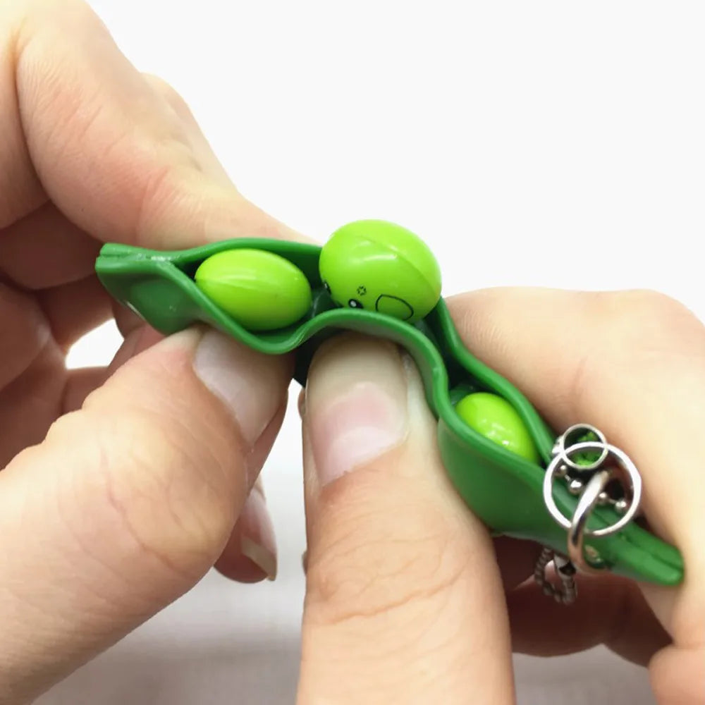 A hand holds a green silicone fidget toy keychain with a small face on it.