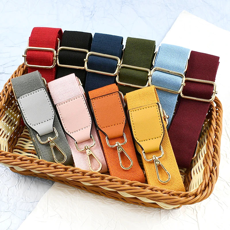 A collection of canvas cotton bag straps in various colors and shades, featuring metal hooks, displayed in a woven basket.