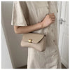 A woman holds a beige leather crossbody bag against a light colored shirt.