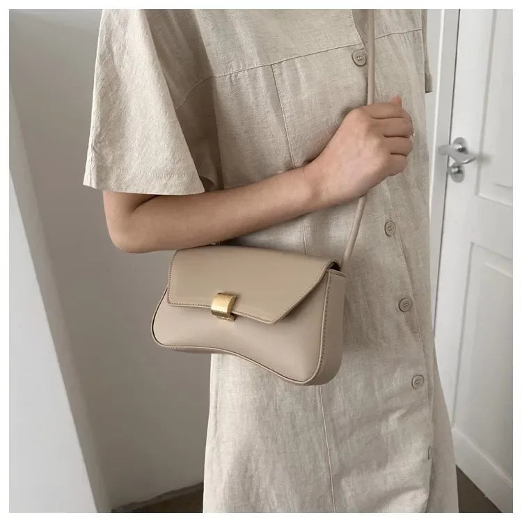 A woman holds a beige leather crossbody bag against a light colored shirt.